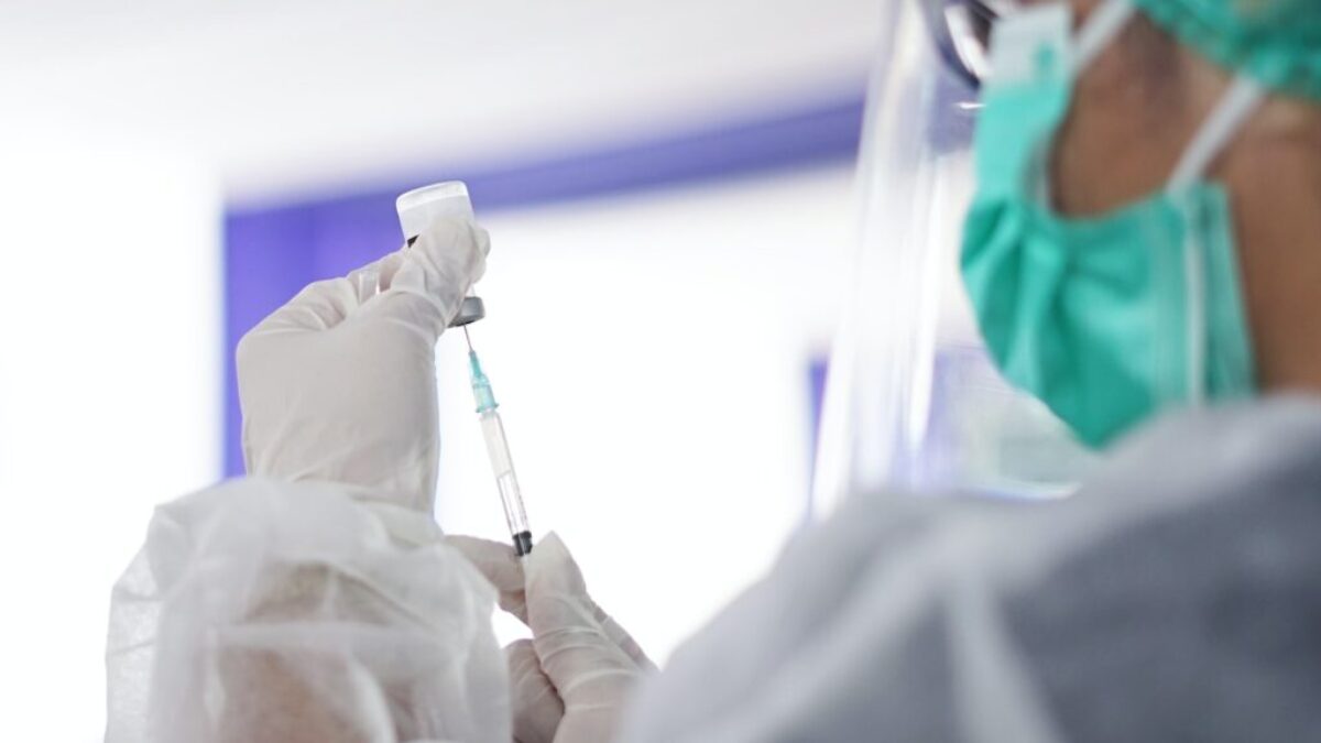 a person in a mask and gloves holding a syringe