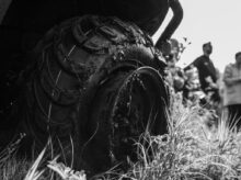 a black and white photo of a group of people looking at a tire