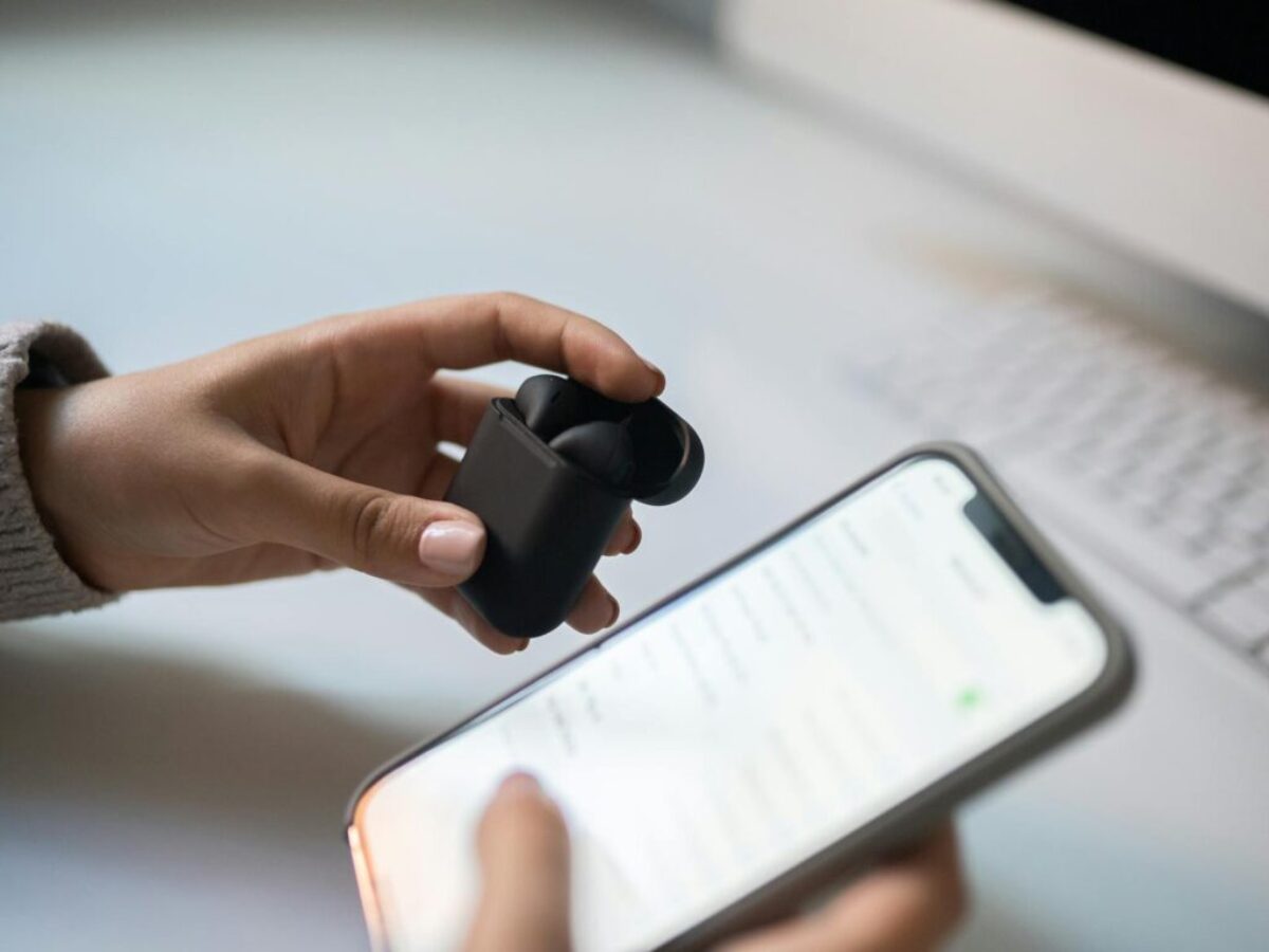 A Person Holding Wireless Earphones and a Smartphone