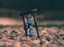 selective focus photo of brown and blue hourglass on stones