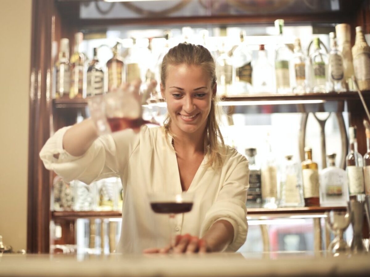 Cheerful female bartender pouring cocktail in bar