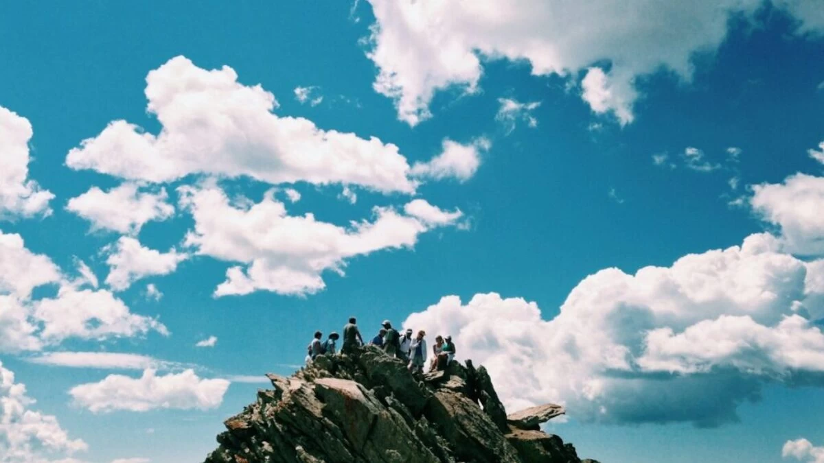 people on rock formation under white cloudy sky