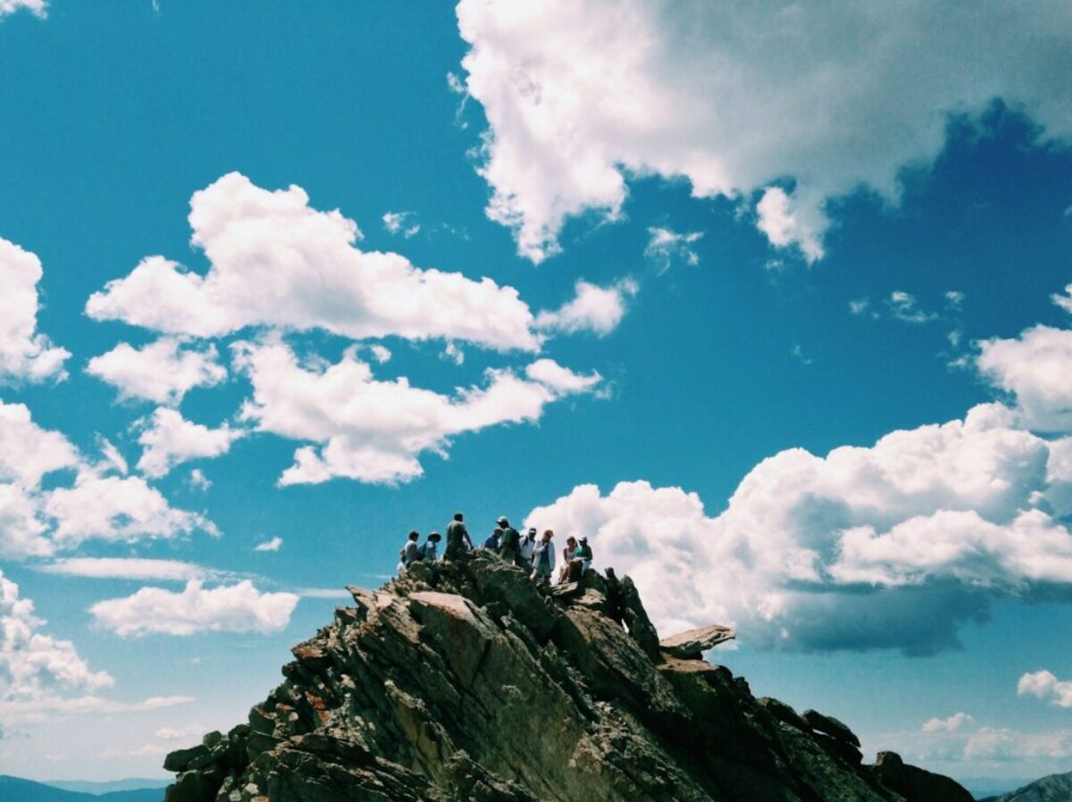 people on rock formation under white cloudy sky