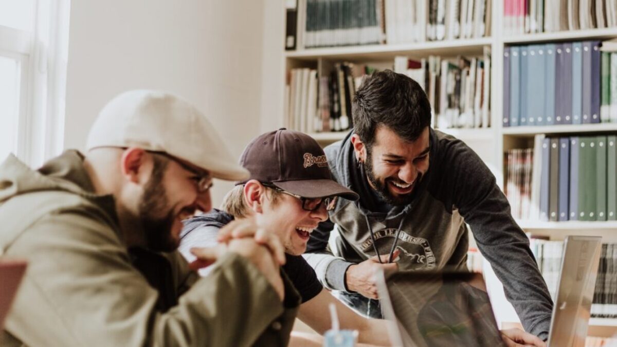 three men laughing while looking in the laptop inside room
