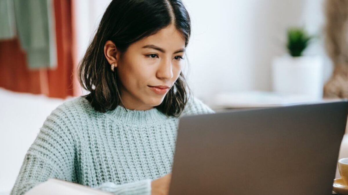 Hispanic woman working remotely on netbook near notebook at home