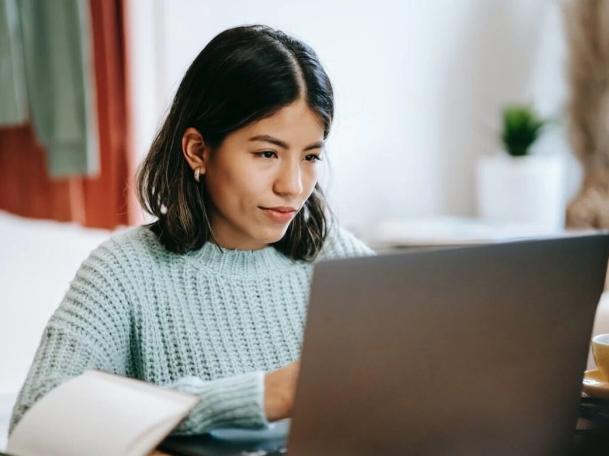 Hispanic woman working remotely on netbook near notebook at home