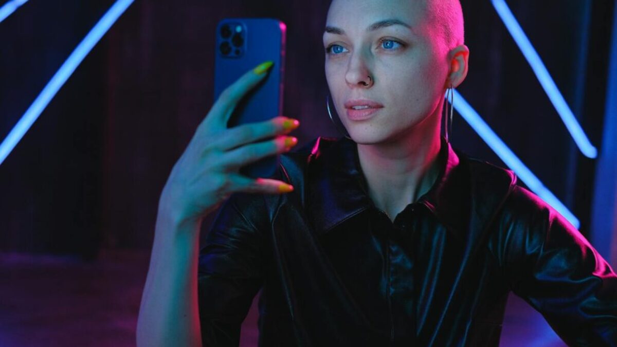 Young Bald woman using photos on smartphone in neon studio