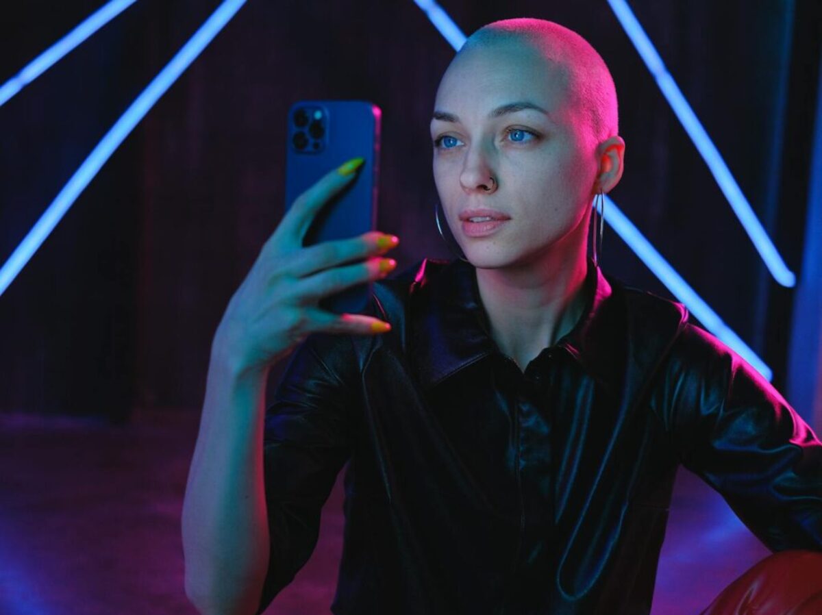 Young Bald woman using photos on smartphone in neon studio