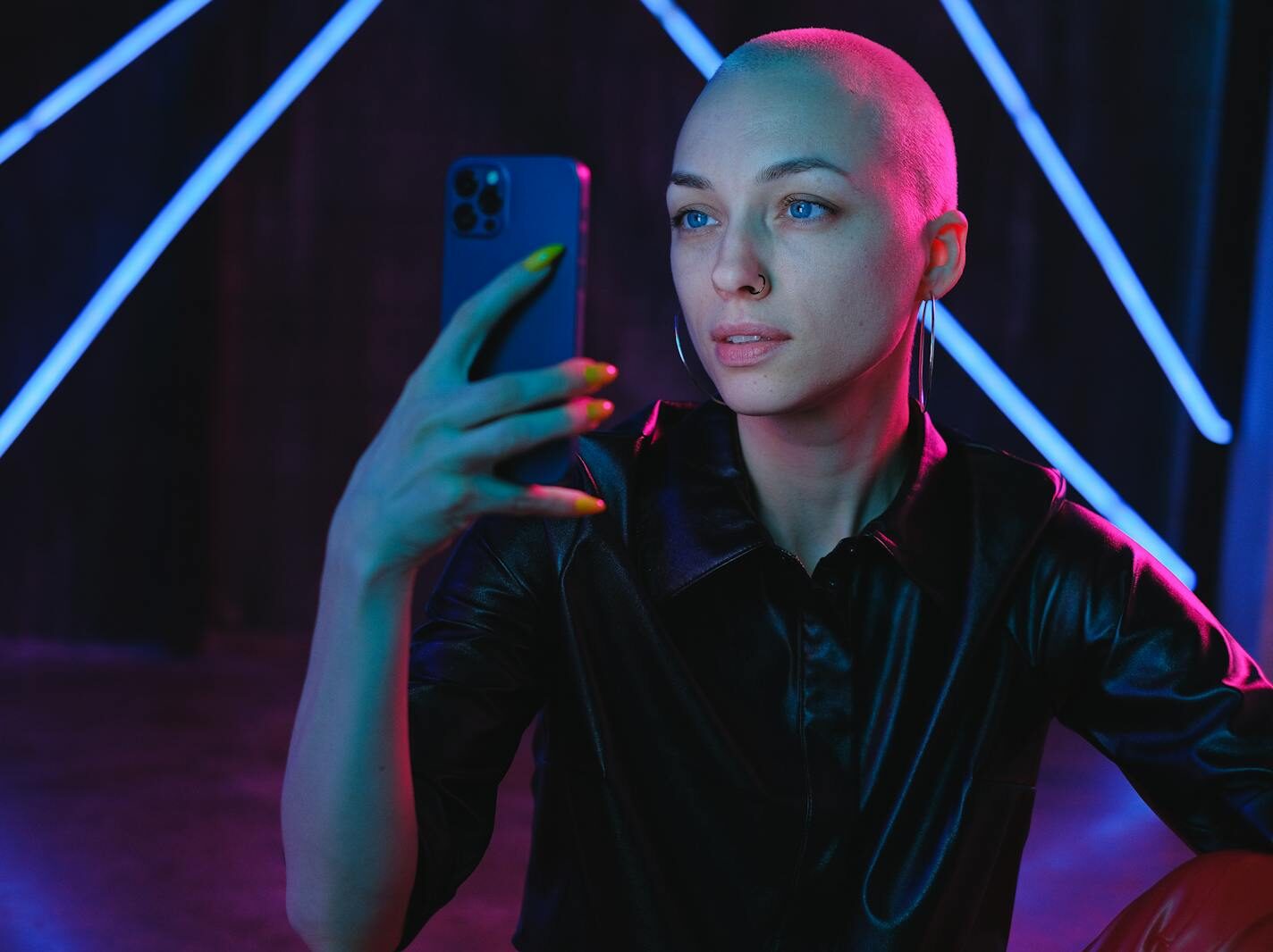 Young Bald woman using photos on smartphone in neon studio