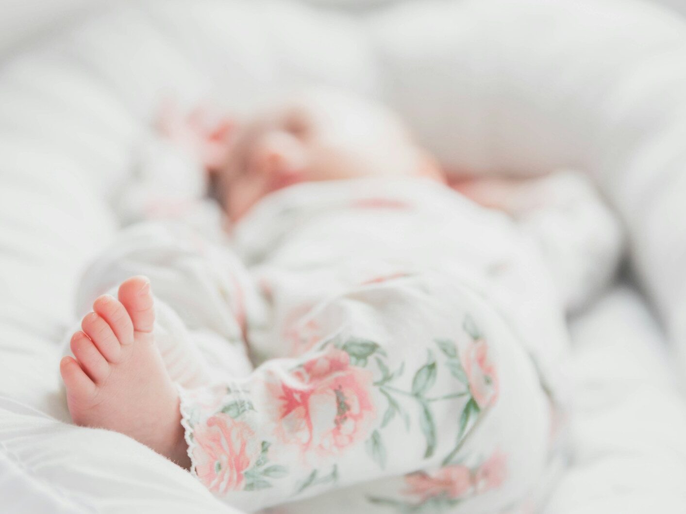baby in white and red floral onesie lying on bed