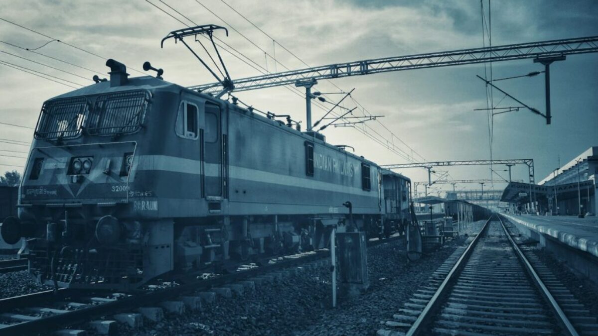 green train on rail tracks under cloudy sky