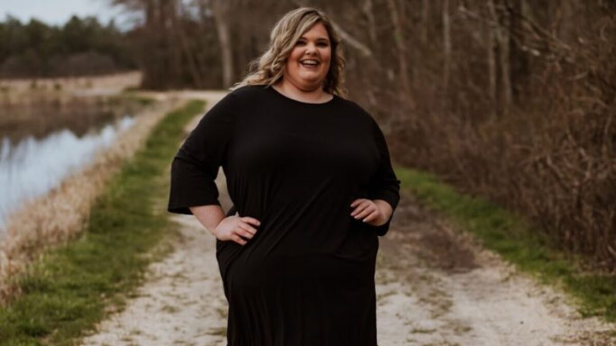 woman in black long sleeve dress standing on gray road near river during daytime