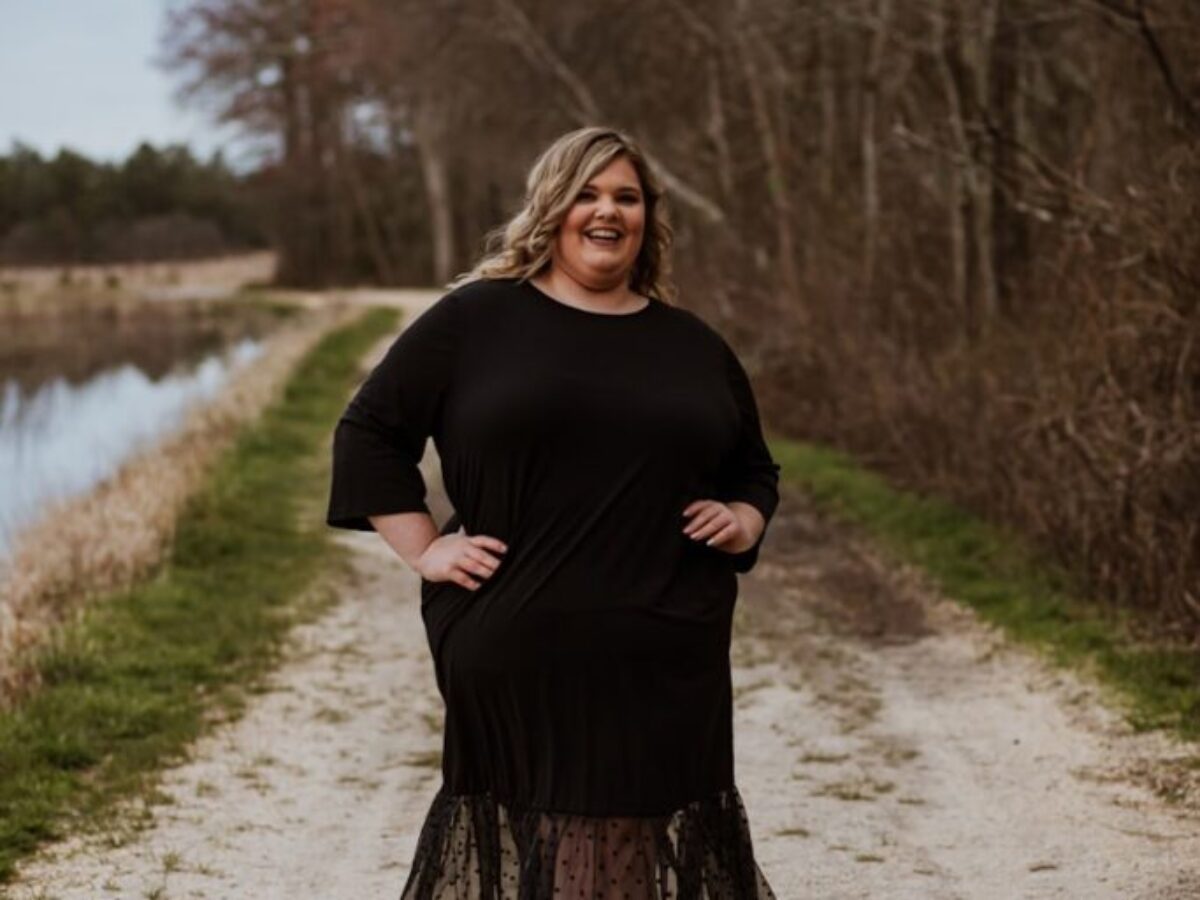 woman in black long sleeve dress standing on gray road near river during daytime