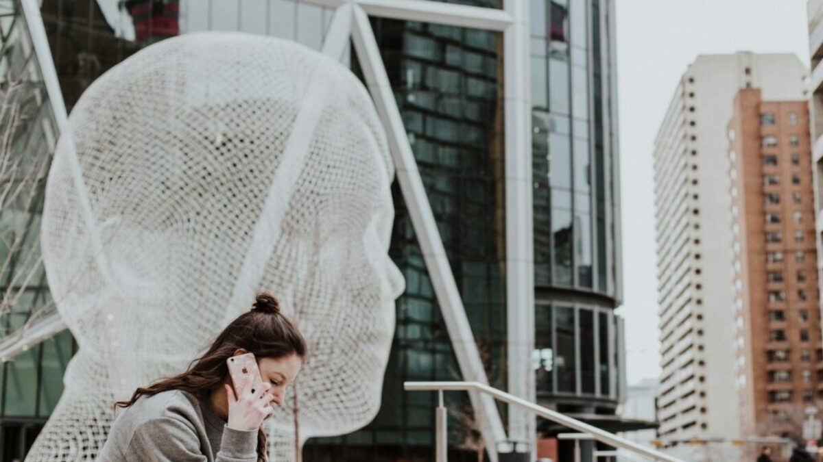 woman sitting on ground holding smartphone near building
