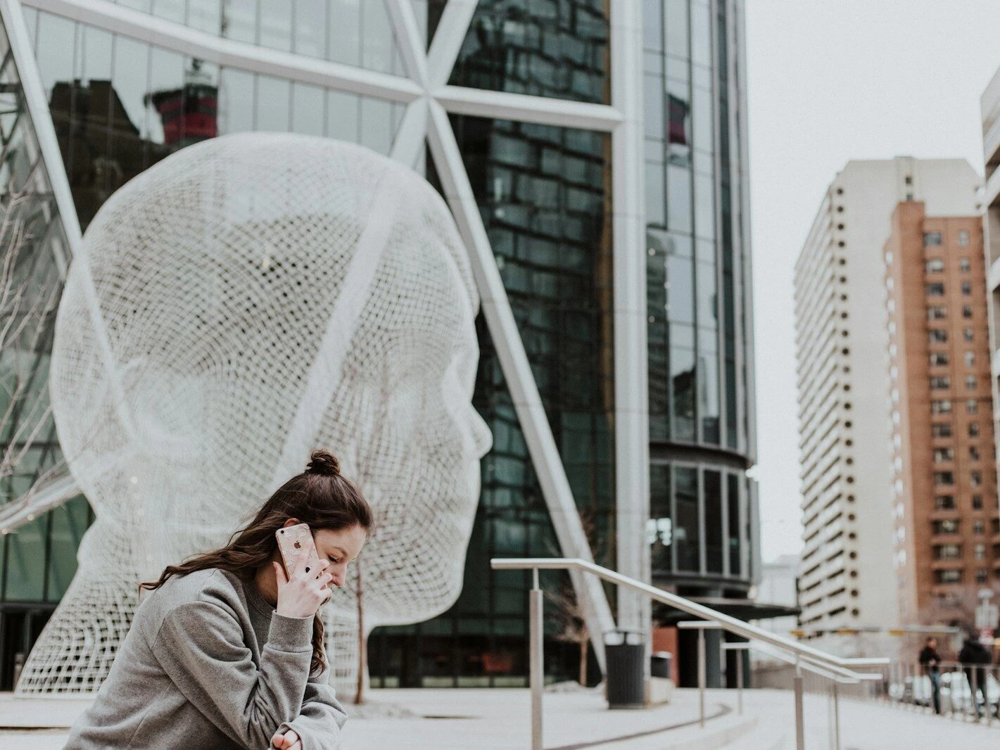 woman sitting on ground holding smartphone near building
