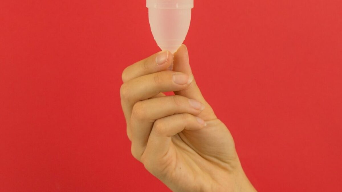 a hand holding a small plastic cup in front of a red background