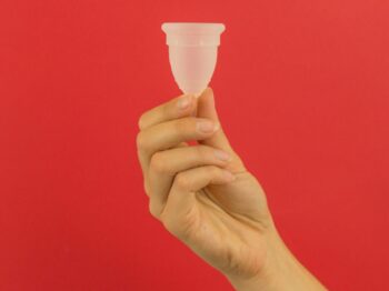 a hand holding a small plastic cup in front of a red background