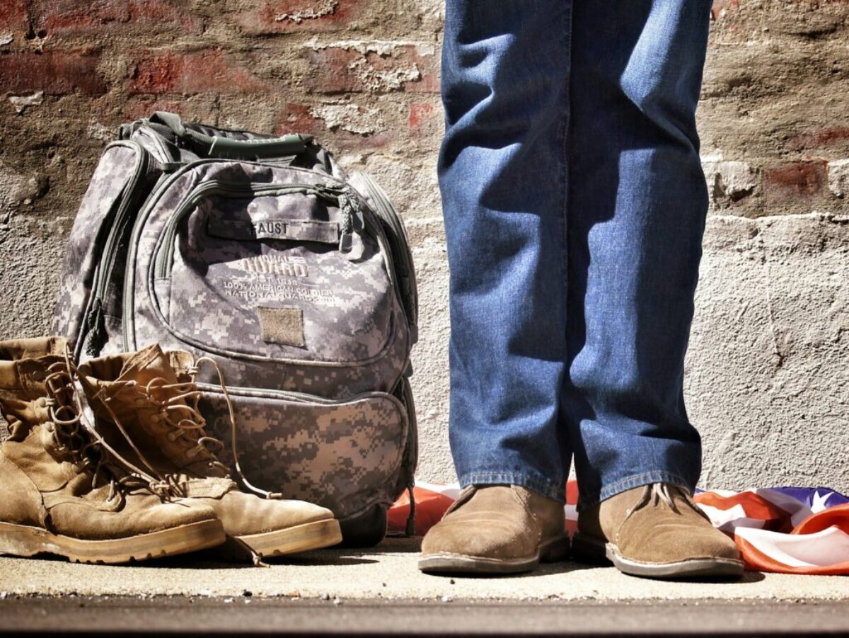 minimalist photography of person standing near backpack and boots