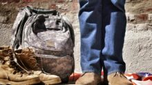 minimalist photography of person standing near backpack and boots