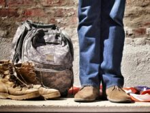 minimalist photography of person standing near backpack and boots