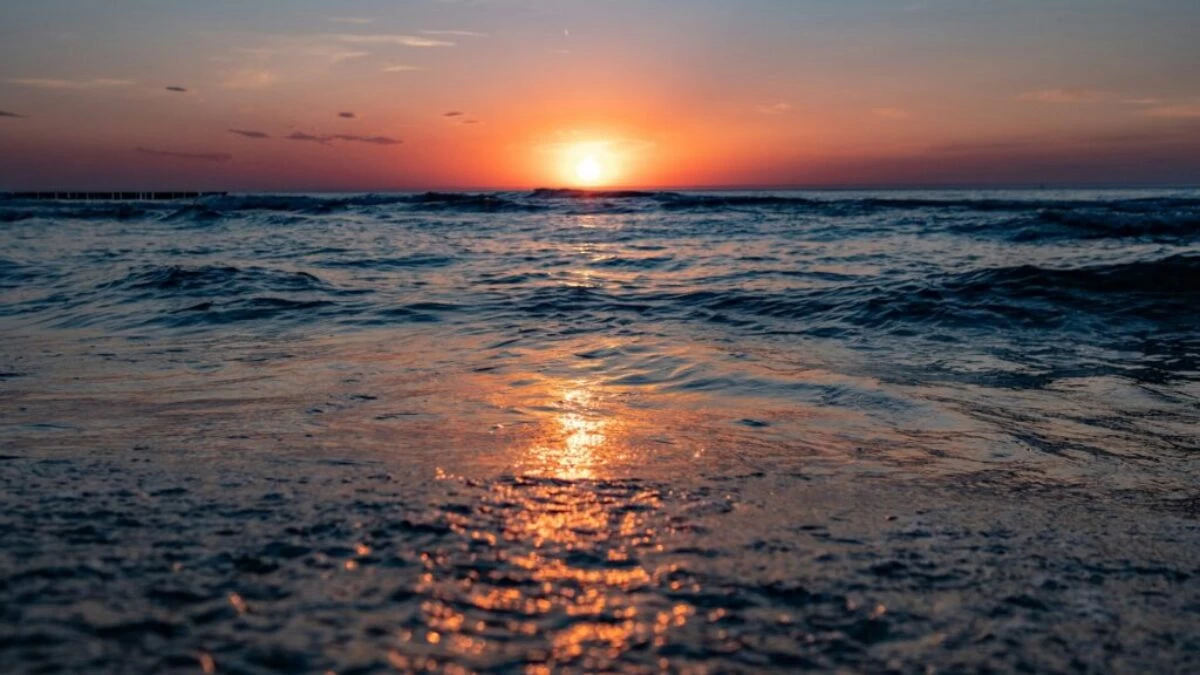 the sun is setting over the water at the beach