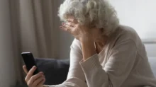 Nešťastná důchodkyně s hlavou v dlani zkoumá informace na telefonu