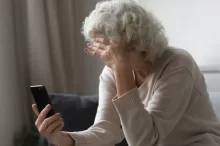 Nešťastná důchodkyně s hlavou v dlani zkoumá informace na telefonu