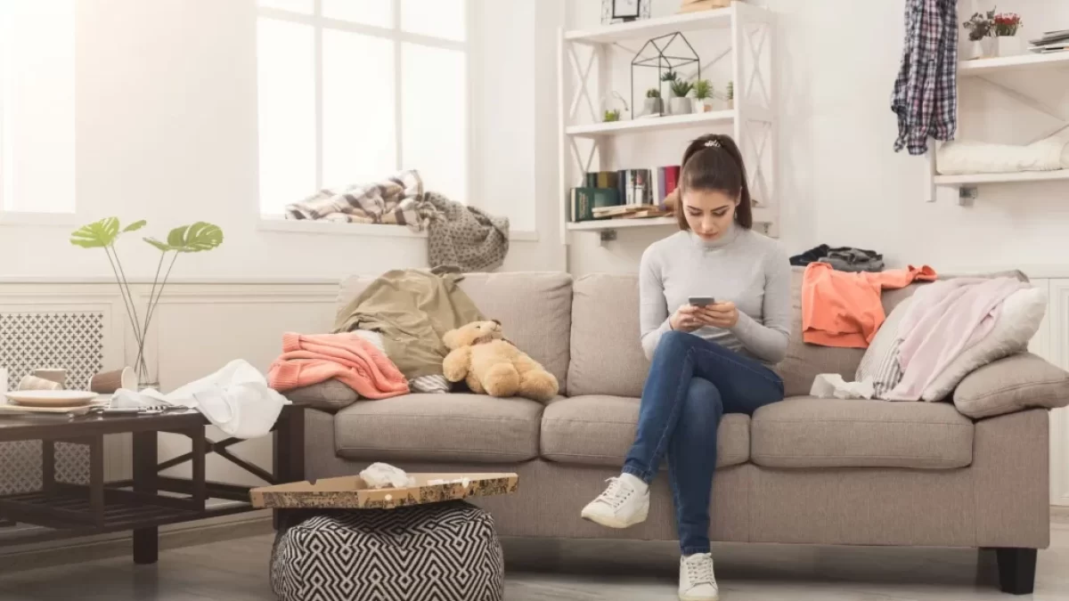 Žena se uprostřed nepořádku doma zabývá mobilem