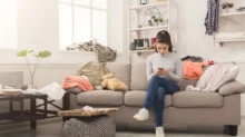 Žena se uprostřed nepořádku doma zabývá mobilem