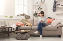 Žena se uprostřed nepořádku doma zabývá mobilem