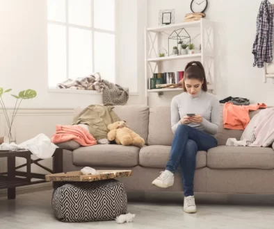 Žena se uprostřed nepořádku doma zabývá mobilem