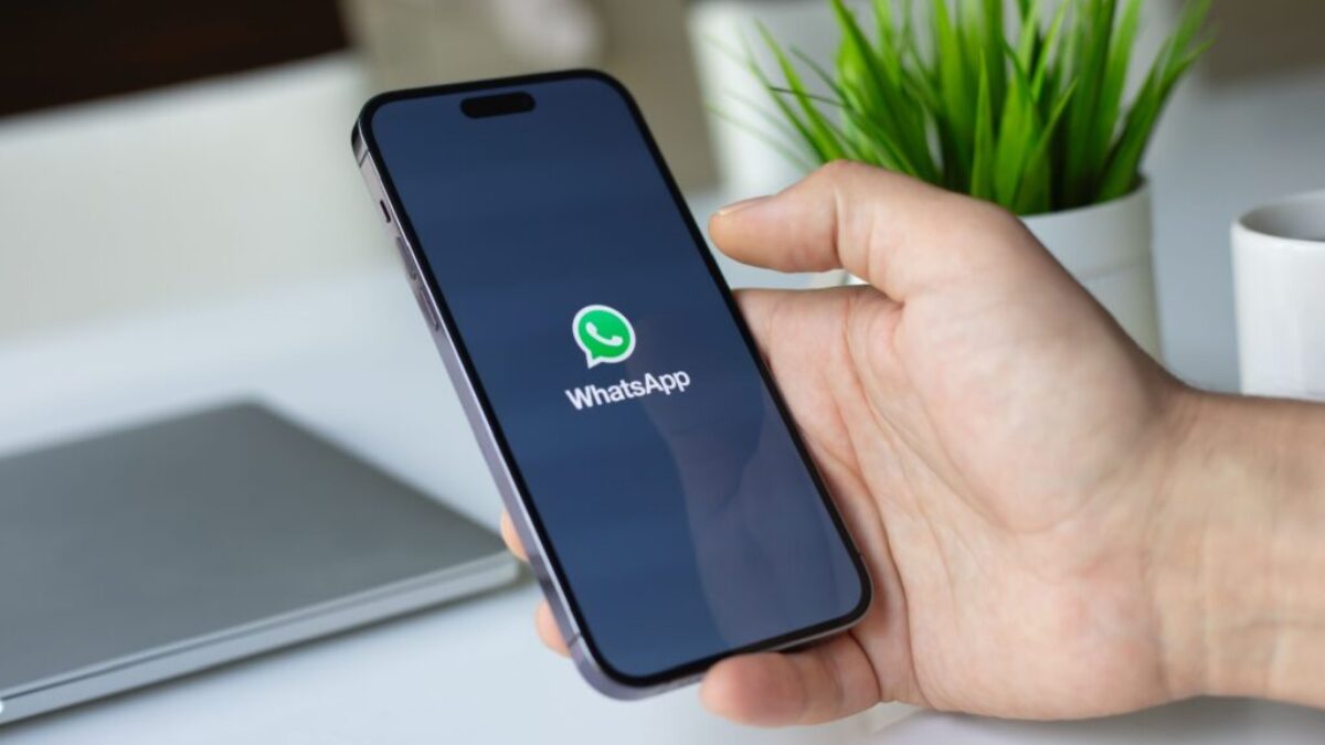 Ruka drží mobilní telefon, na kterém se spouští aplikace WhatsApp