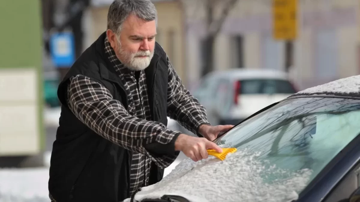 Muž sundává z čelního skla sníh