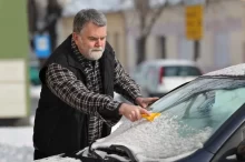 Muž sundává z čelního skla sníh