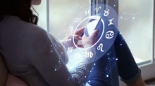 horoskop, žena sedí u okna a dívá se do telefonu