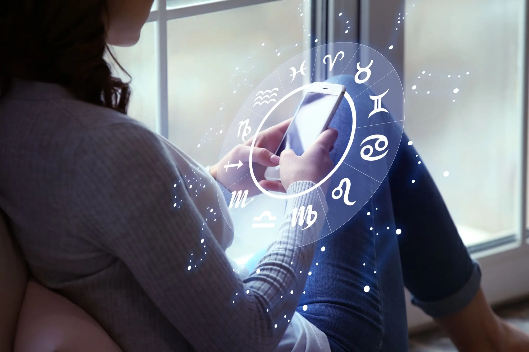 horoskop, žena sedí u okna a dívá se do telefonu