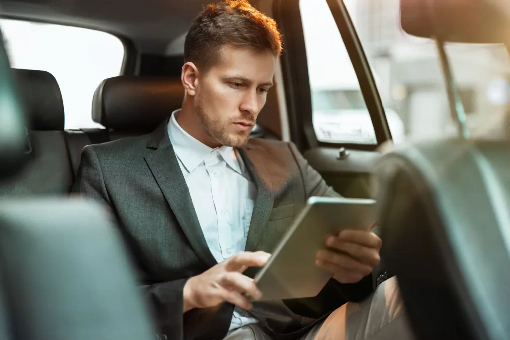 muž sedí v autě a pracuje na tabletu