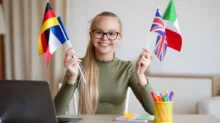 polyglotka, dívka sedí u počítače s různými vlajkami v rukou
