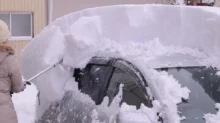 Žena odhrabuje sníh z auta
