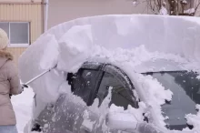 Žena odhrabuje sníh z auta