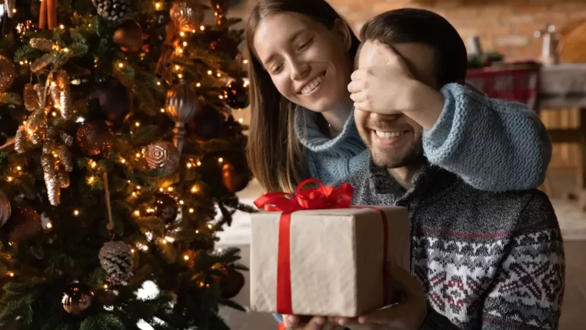 Žena dává dárek svému partnerovi u vánočního stromku