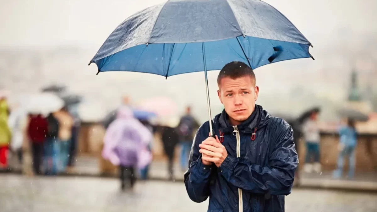 Muž v dešti stojí pod deštníkem.