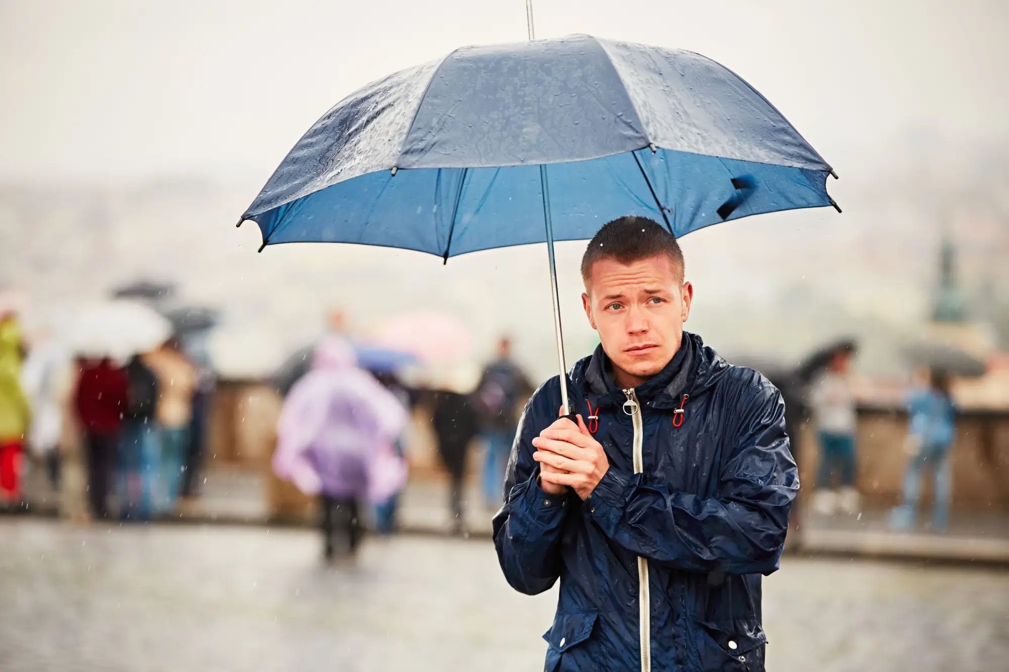 Muž v dešti stojí pod deštníkem.