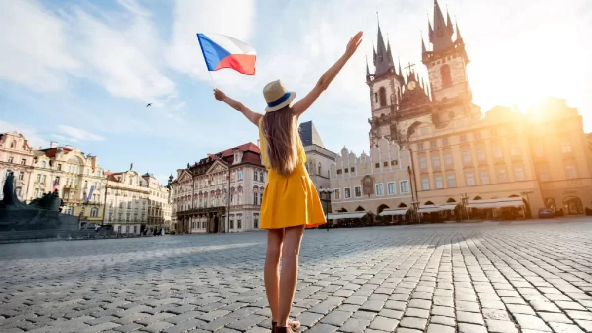 Mladá žena v šatech drží českou vlajku