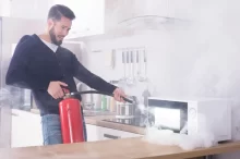 Muž hasí mikrovlnku hasícím přístrojem