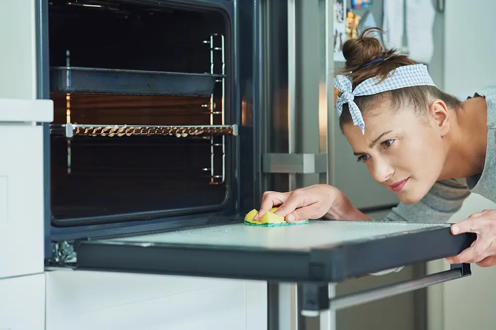 Pomocí houbičky naneste pastu na sklo trouby a nechte působit alespoň 15 minut. - Techsvět žena čistí sklo trouby