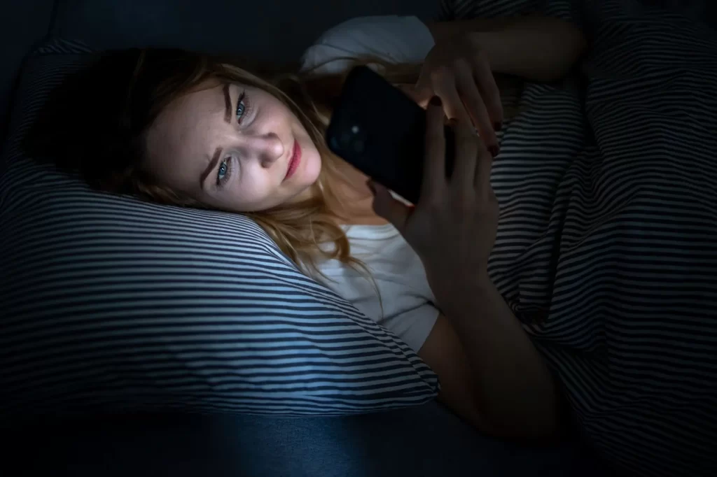 shutterstock_2302942047 - Techsvět Žena v posteli se dívá do mobilu.