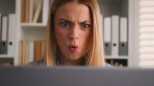 Žena šokovaně zírá do počítače.