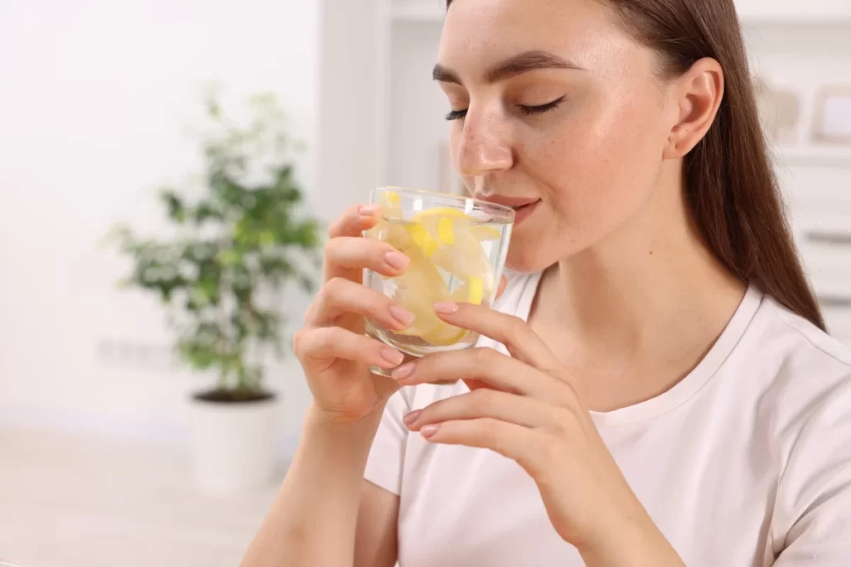Žena, která pije vodu s citrónem.
