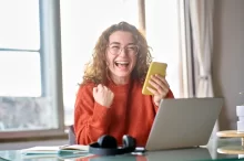 žena u počítače s mobilem v ruce se raduje z výhry